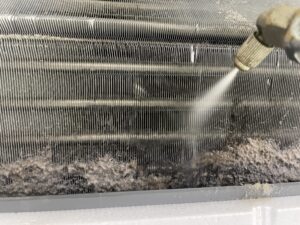 八幡市の施設にてエアコン内部の分解高圧洗浄を行っている作業風景。フィンに分厚くこびりついたホコリと黒カビを、プロ専用の機材で一気に洗い流している様子