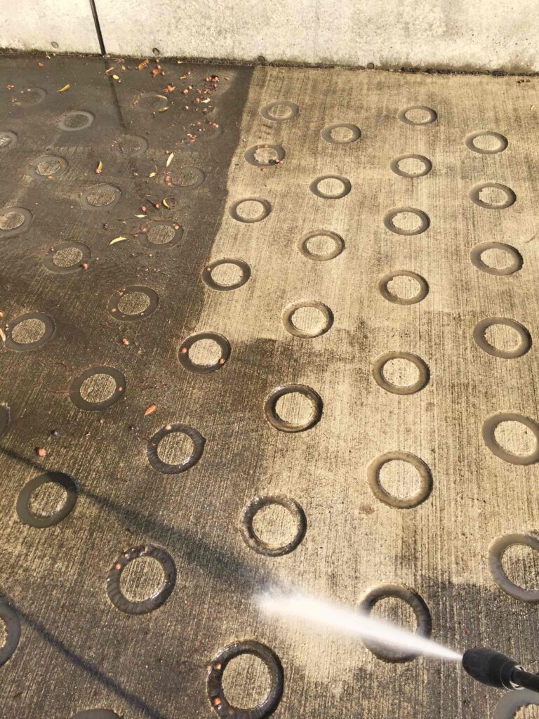 京都府の施設にて、黒ずんで滑りやすくなった駐車場スロープを高圧洗浄で清掃している様子。スリップ事故防止のためのメンテナンス風景